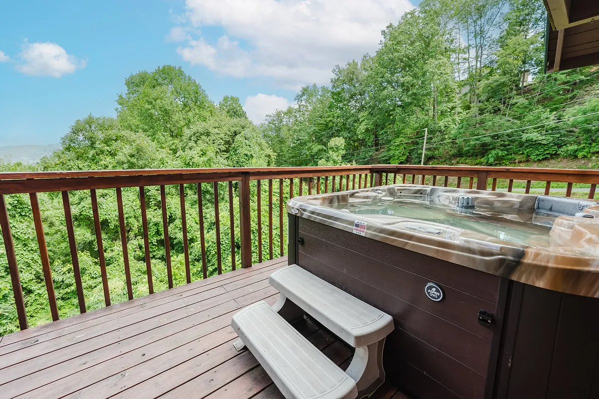 A cozy deck with a bubbling hot tub overlooks lush trees, framed by classic wooden railings. The scene invites guests to unwind after a day of adventure, offering tranquil moments and the chance to enjoy nature from the comfort of the cabin.