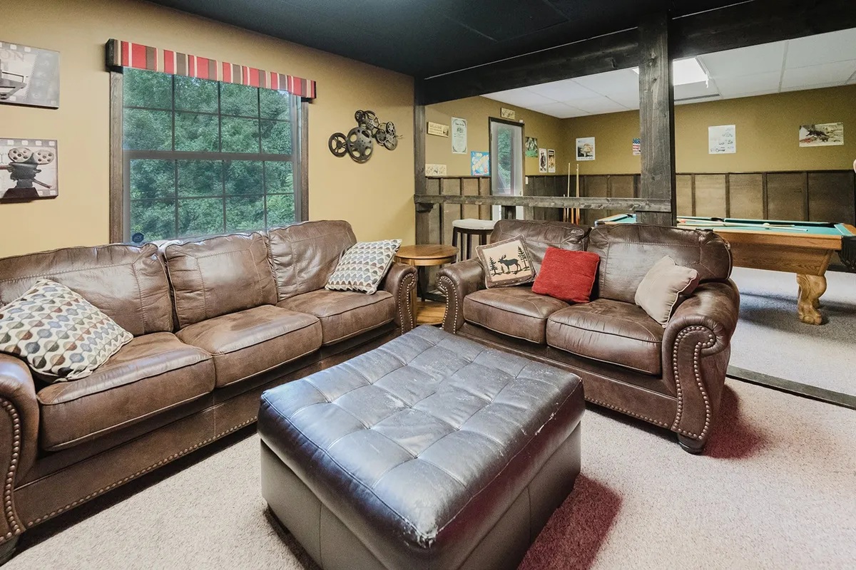 A relaxed entertainment space featuring leather couches, a coffee table, and a pool table visible in the background. The open layout encourages socializing, conversation, and friendly gaming.