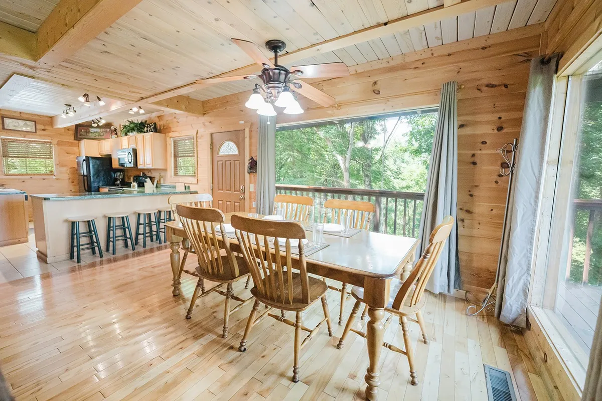 A bright dining area with a large wooden table and chairs, complemented by big windows and an adjacent kitchen island. Natural light fills the space, making it ideal for family dinners, game nights, or quiet mornings with coffee.