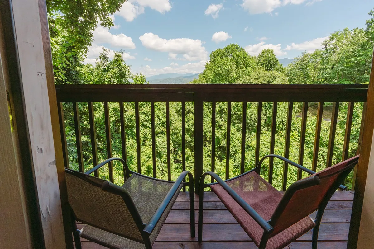 Two comfortable chairs are positioned on a wooden deck, overlooking a lush landscape with expansive mountain vistas. The setting is ideal for sipping coffee, reading a book, or enjoying the sunset, with the inviting tranquility of the Smokies as a backdrop.