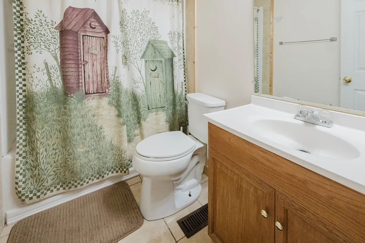 A well-kept shared bathroom with a rustic shower curtain, wooden vanity, and toilet, providing a clean, practical, and inviting space for personal care and refreshment.