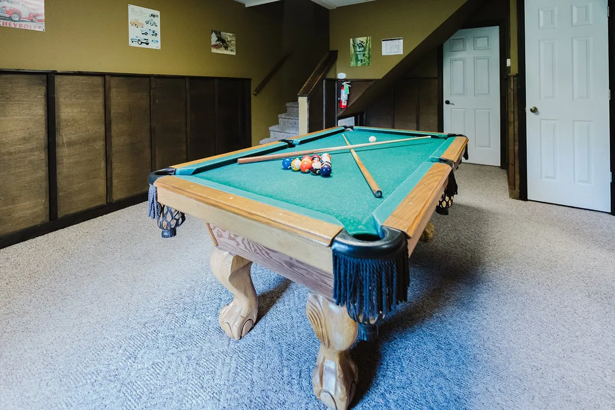 A vibrant game room featuring a pool table, staircase, and colorful wall art. The space is set up for group fun and friendly competition, perfect for socializing and making memories during any season.