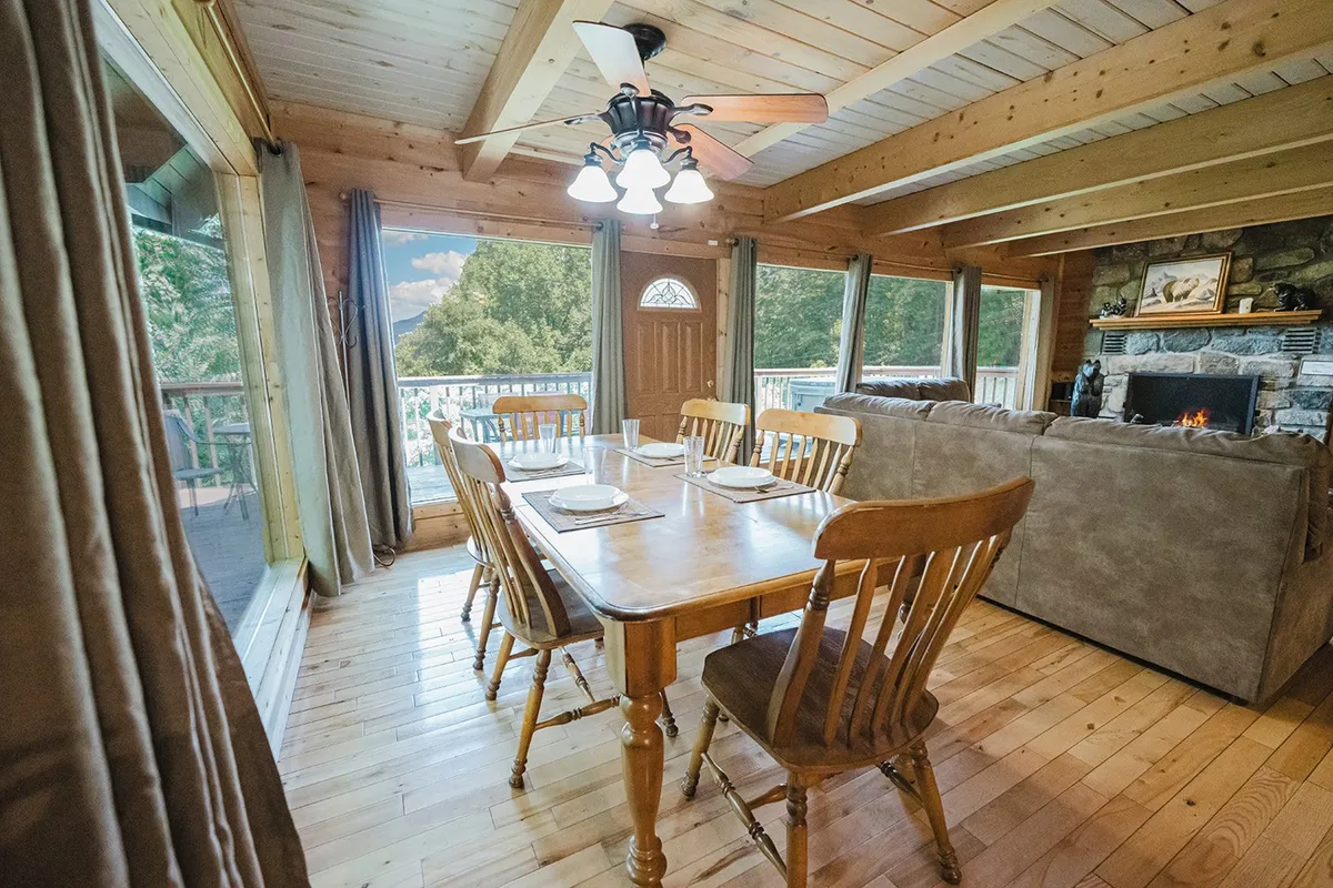 A warm and welcoming dining area anchored by a stone fireplace and surrounded by large windows, creating an inviting space for family dinners, game nights, or relaxing with friends. Natural light streams in, enhancing the cozy, communal atmosphere.