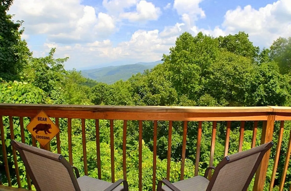 A panoramic view of the mountains seen from the deck, with deck railing and comfortable chairs setting the scene for morning coffee or group conversations amid nature. The expansive vista captures the tranquil beauty of the Smoky Mountains, inviting relaxation and shared moments outdoors.