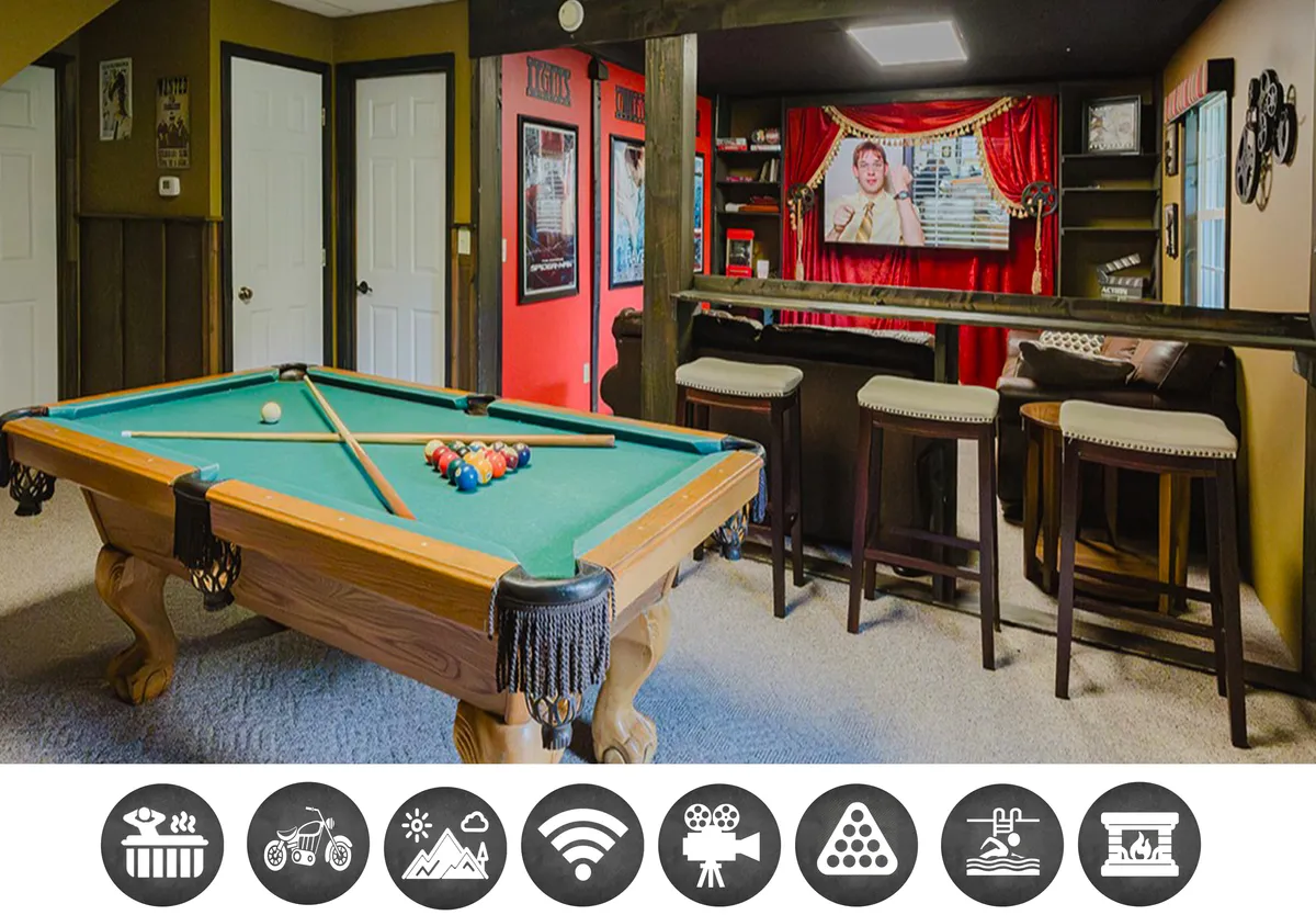 The image showcases a vibrant, inviting interior lounge space at Bearly Hidden Ridge cabin. Central to the scene is a classic pool table, surrounded by a cozy bar area perfect for gathering, and a movie-viewing zone with plush seating, rich red curtains, and retro posters adding character. The warm wooden architecture and relaxed lighting create an atmosphere ideal for fun, laughter, and shared experiences with family or friends.